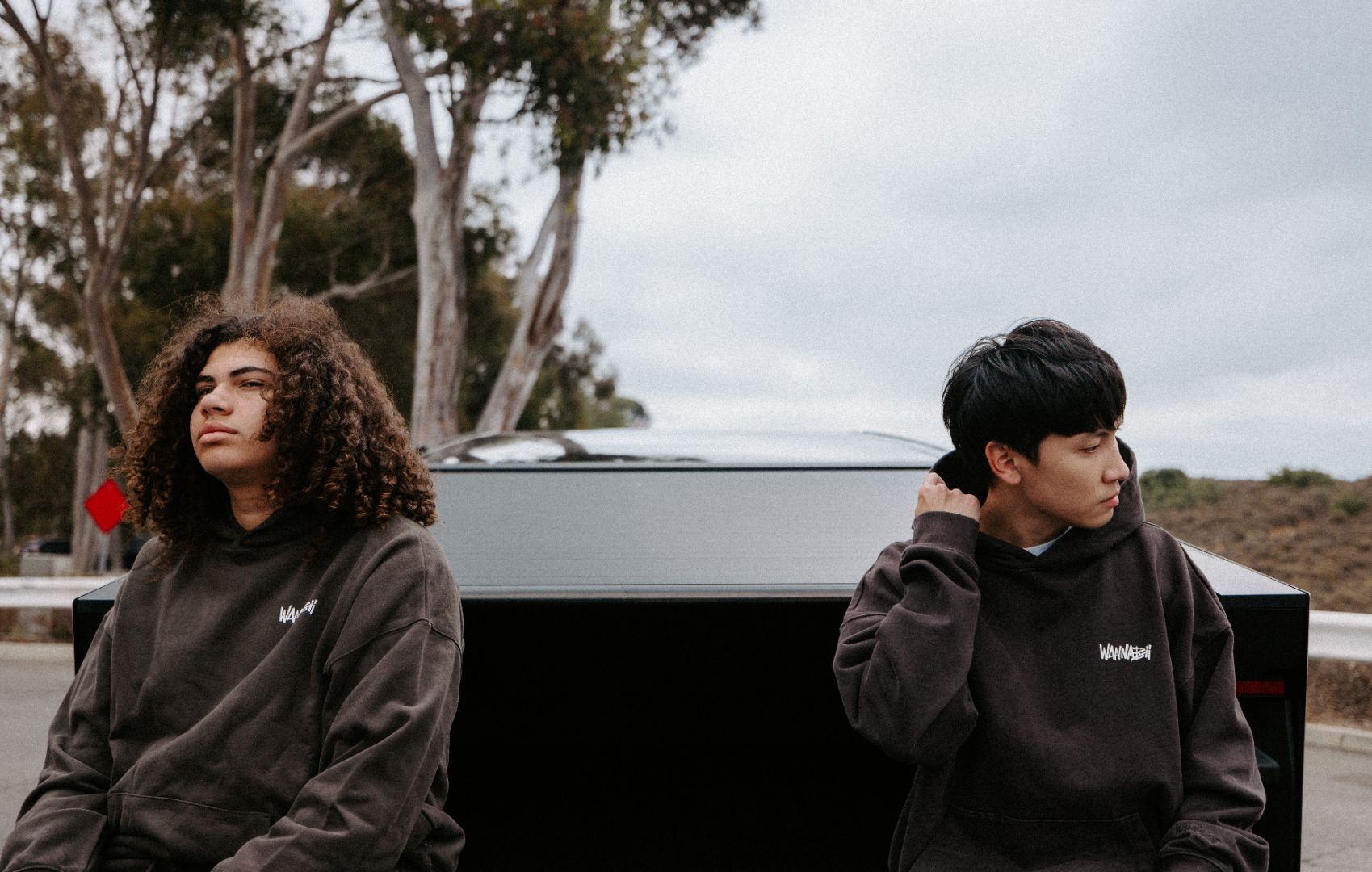 Two individuals wearing hoodies with visible branding sitting outdoors.